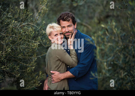 Young affectionate couple standing outdoors in olive orchard, hugging. Stock Photo