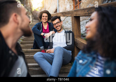 A portrait of group of young friends sitting outdoors on staircase in town. Stock Photo