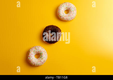 pink white and black chocolate donuts on yellow background top view Stock Photo