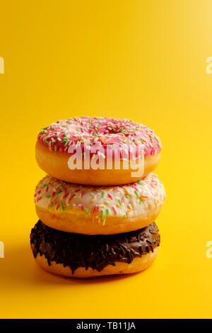 pink white and black chocolate donuts on yellow background Stock Photo