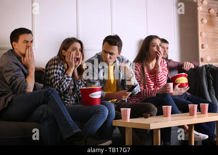 Group of friends eating nuggets while watching horror movie on TV at home Stock Photo