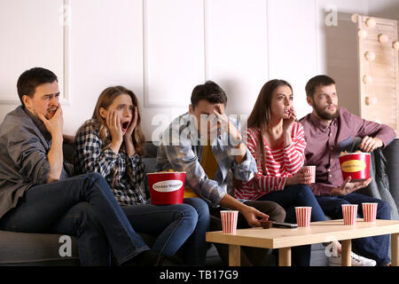 Group of friends eating nuggets while watching horror movie on TV at home Stock Photo