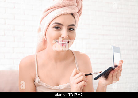 Young woman after shower applying cosmetics onto face at home Stock Photo