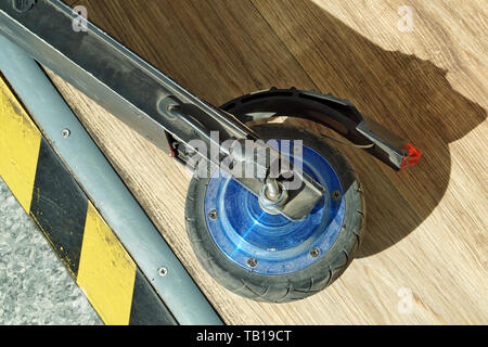 Broken wheel of a small modern electric scooter on the background of a wooden floor Stock Photo