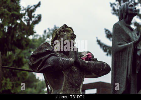 The granite statue of a woman praying with the rose in her hand in the monumental cemetery of Cremona. Stock Photo