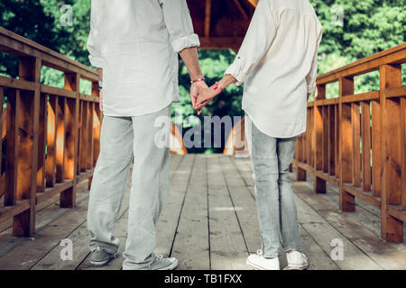 Close-up of spouses holding hands while standing on the bridge. Stock Photo
