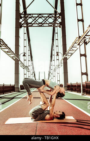 Yogi supporting his partner while doing acroyoga outdoors Stock Photo