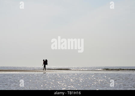 Amazing silhouette of a male backpackers walking across the shallow water on the beach in summer sunshine Stock Photo