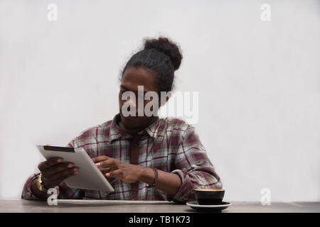 a young black man using tablet and smartphone with glass of coffee, a papua young man using tablet with a coffee cup Stock Photo