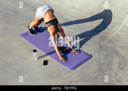 fitness woman practising downward facing dog yoga pose. Female in sportswear doing stretching workout outdoors. Stock Photo