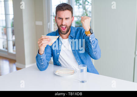 Handsome man eating healthy sandwich annoyed and frustrated shouting with anger, crazy and yelling with raised hand, anger concept Stock Photo