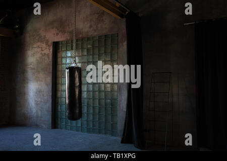 Black punching bag in dark grunge gym. Fitness Boxing and martial arts, copy space. Stock Photo