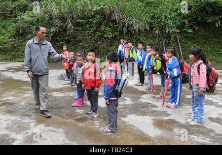 (190529) -- RONGSHUI, May 29, 2019 (Xinhua) -- Zhou Hongjun reaffirms safety regulations as students listen after school in Dayou primary school in Xinhe village, Rongshui Miao Autonomous County, south China's Guangxi Zhuang Autonomous Region, May 28, 2019. Zhou Hongjun, a teacher of 46 years' experience, works in a school  since he was 16 in the remote rural area in Rongshui Miao Autonomous County. Before 2010, there wasn't road access to the school, all school supplies were taken by Zhou himself with a carrying pole. Zhu, supposed to retire in 2018, decided to continue his career as there wa Stock Photo