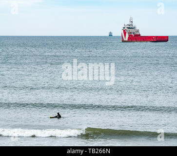 Aberdeen, Scotland, United Kingdom, 29th May 2019. UK Weather:  A man surfing in the waves at the beach near Footdee with offshore supply ships at sea on the horizon Stock Photo