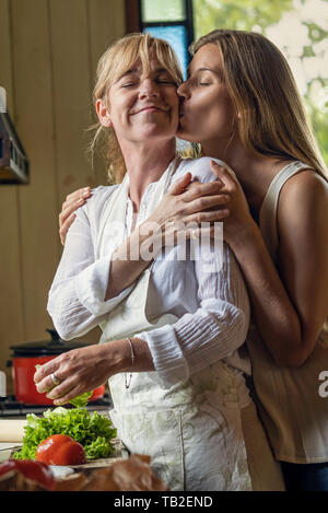 Daughter kissing her mother in kitchen Stock Photo