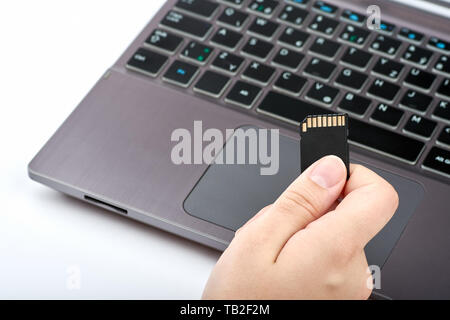 View of a woman holding a black SD card in her hand. Silver laptop or computer with black keyboard, isolated on white background Stock Photo