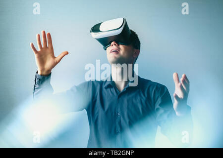 Young man in virtual glasses interacts with virtual reality and makes gestures. Stock Photo