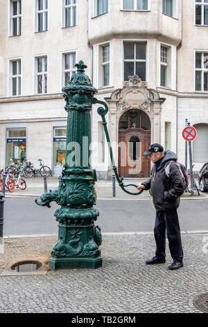 Schöneberg-Berlin. Elderly man using ornate old water pump in front of  Historic listed building on Viktoria Luise Platz Stock Photo