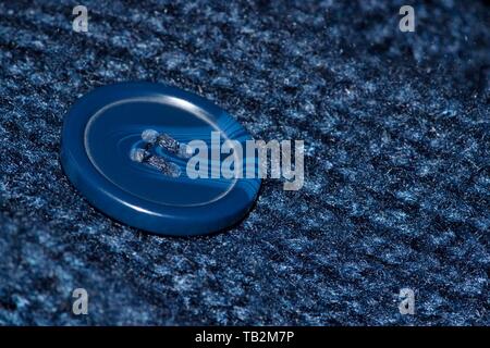 Macro image of a plastic blue button sewn into a navy blue cardigan. Button is off center and angled. Stock Photo