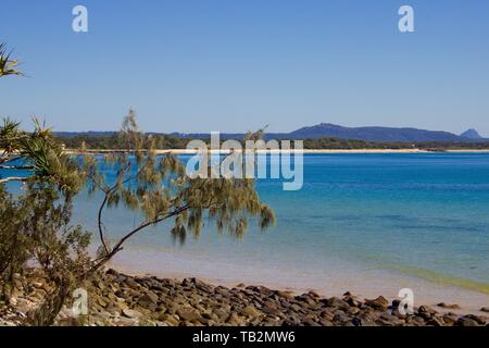 Beautiful tranquil beach scene in Noosa, Queensland Australia showing turquoise blue water with rocks in foreground Stock Photo