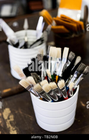 High angle close up of white ceramic pot with selection of paintbrushes in various sizes.
