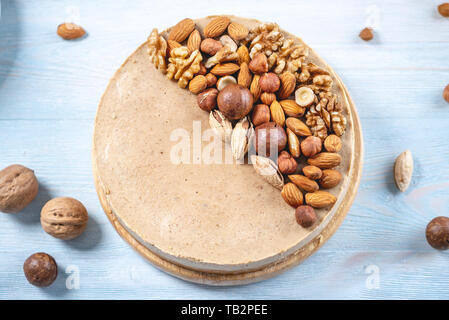 Nutty caramel cheesecake cake with topping of walnut, almond, hazelnut and macadamia on a blue wooden background. Homemade nut dessert. Stock Photo
