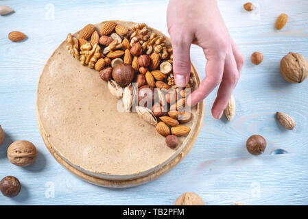 Nutty caramel cheesecake cake with topping of walnut, almond, hazelnut and macadamia on a blue wooden background. Homemade nut dessert. Stock Photo