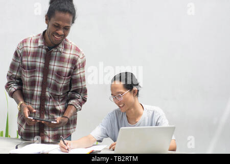 two friend with diffrent ethnic working together with laptop and tablet discussing something, two young man working and studying together Stock Photo
