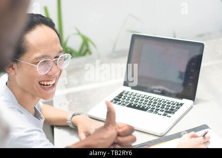 coworkers give thumb up at friend, young asian man with glasses with laptop and notebook get thumb up from friend Stock Photo