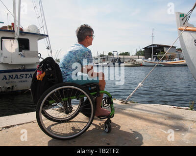 Disabled woman in wheelchair enjoys the view of the Anclote River from the sponge docks in Tarpon Springs, Florida, USA, May 9, 2019, © Katharine Andr Stock Photo
