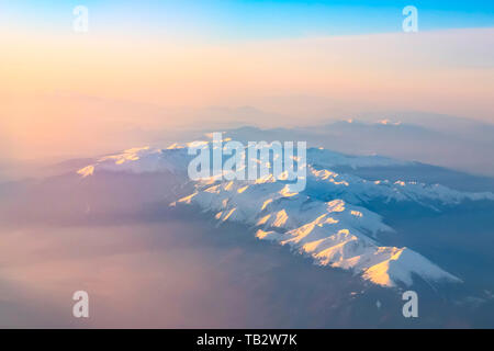 Aerial view of colorful sunrise over mountains snow peaks and silhouettes, shot from airplane Stock Photo