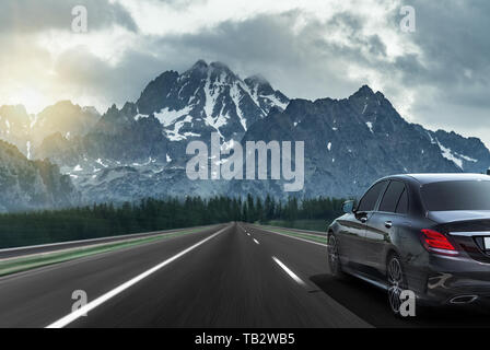 The car drives fast on the highway against the backdrop of a mountain range. Stock Photo