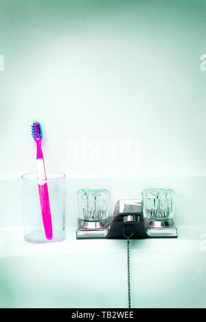 A pink toothbrush in a glass cup on the sink counter. Stock Photo