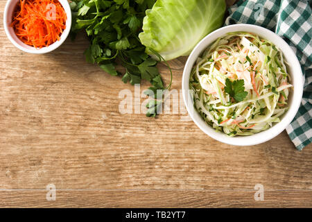 Coleslaw salad in white bowl and ingredients on wooden table Stock Photo