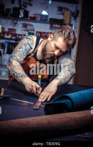 Professional Leather Worker cutting out leather goods at his work area. Stock Photo