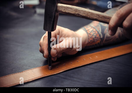 Handicraftsman processing a leather workpiece at the workshelf Stock Photo