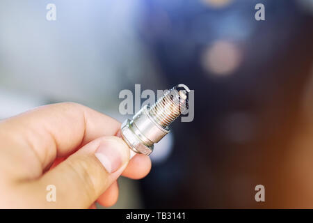 Machanic hand holding used dirty spark plug with disassembled boat engine on background during repair. Seasonal motor service and maintenance Stock Photo