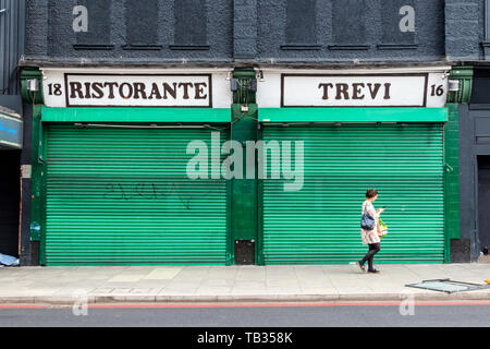 A woman walking past Ristorante Trevi, an Italian restaurant at Highbury Corner, closed with its green-painted metal shutters down, London, UK Stock Photo