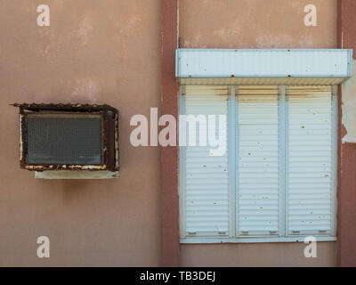 Old window air conditioner and window with closed rolling shutter. Stock Photo