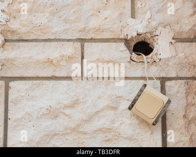 White brick wall with light switcher hanging on the electric cable. Abandoned house, urban decay concept. Stock Photo