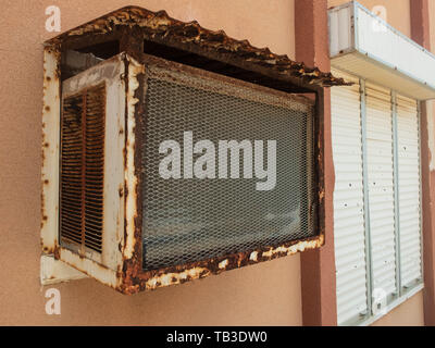Old window air conditioner and window with closed rolling shutter. Stock Photo