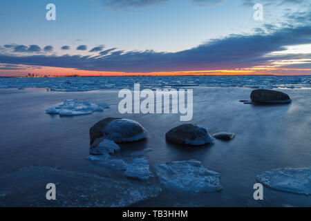 Sunset over frozen coast of the Baltic sea. Calm winter moment. Icy boulders on the blue background. Stock Photo