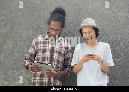 two man using smartphone, asian and black man best friend using smartphone and tablet Stock Photo