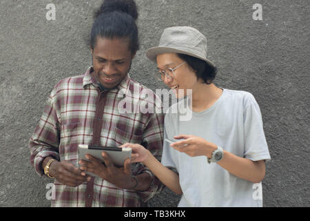 two man using smartphone, asian and black man best friend using smartphone and tablet Stock Photo