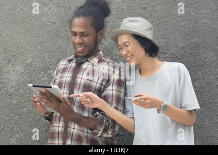 two man using smartphone, asian and black man best friend using smartphone and tablet Stock Photo