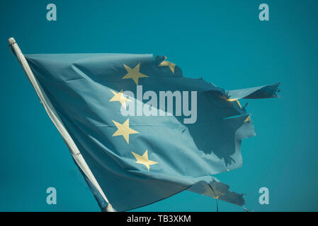 Euro skepticism concept. Torn EU flag wave on blue sky. European Union flag with twelve stars on sunny outdoor. Symbol of unity. Stock Photo