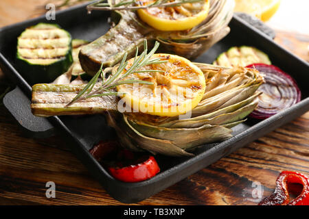 Pan with tasty grilled artichokes and vegetables on wooden table Stock Photo