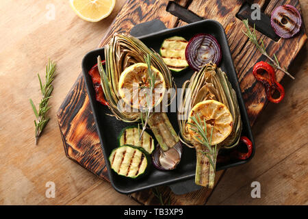 Pan with tasty grilled artichokes and vegetables on wooden table Stock Photo