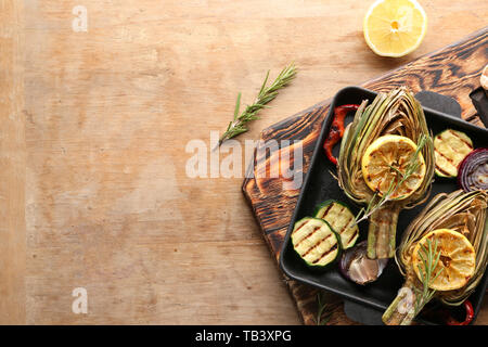 Pan with tasty grilled artichokes and vegetables on wooden table Stock Photo