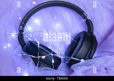 Headphones laying on purple tulle and led lights around them Stock Photo